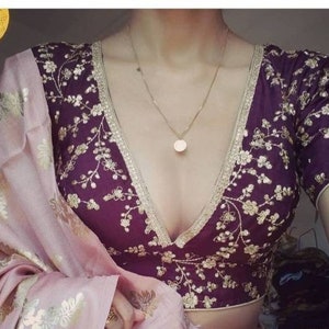 May include: A purple embroidered blouse with a deep V-neckline and gold floral embellishments. The blouse has a short sleeve and is trimmed with a gold lace.