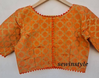 May include: Orange blouse with a gold geometric pattern. The blouse has short sleeves and is trimmed with orange zigzag edging along the neckline, hem, and sleeve cuffs. The front closure features small orange pom-poms. The text "sewinstyle" is visible.