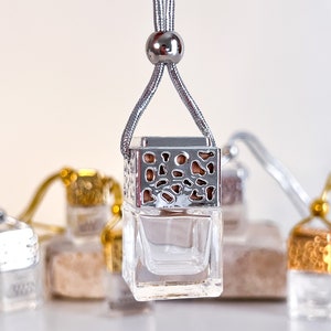 May include: A silver car air freshener with a decorative metal cage and a clear glass bottle. The air freshener is hanging from a silver cord with a silver bead.