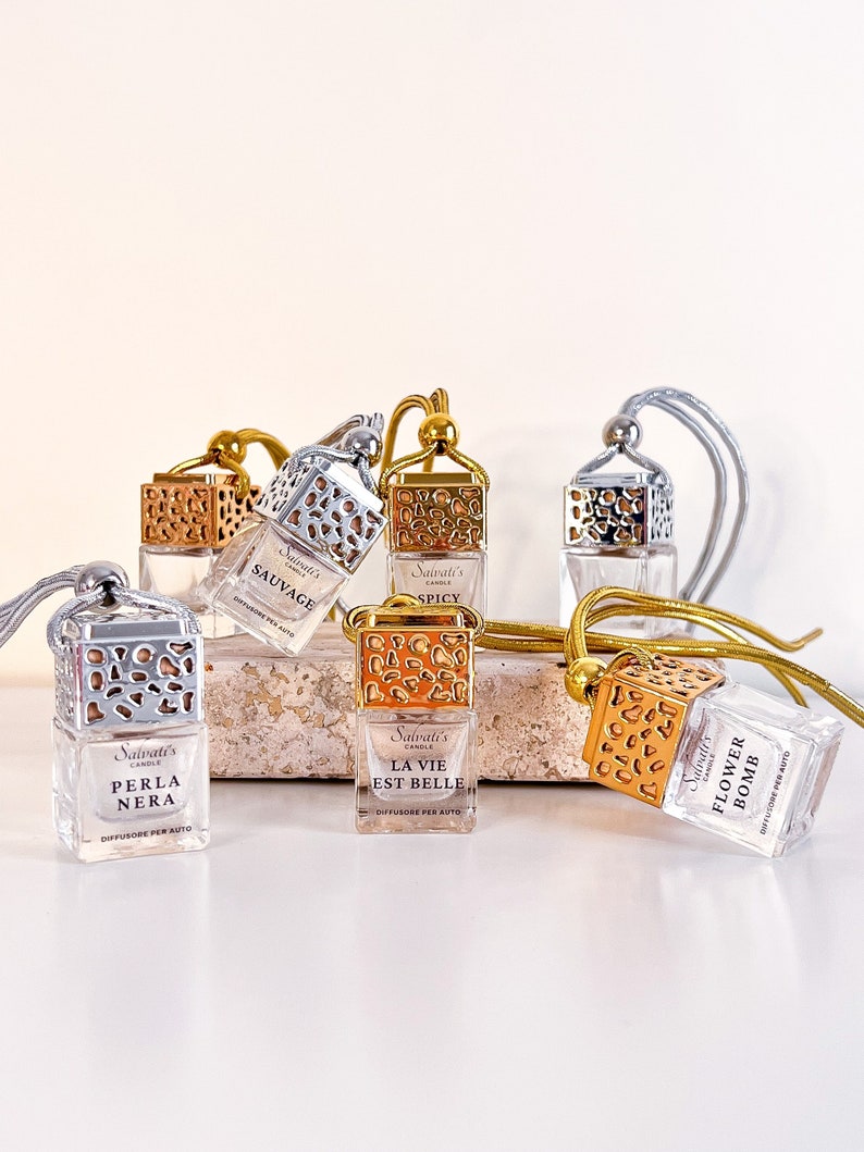 May include: Six gold and silver car air fresheners with different scents. The scents are: Sauvage, Spicy, Perla Nera, La Vie Est Belle, Flower Bomb. Each air freshener has a gold or silver metal cage with a decorative pattern and a string for hanging.