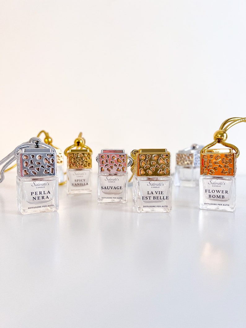 May include: Five small glass bottles with gold lids and decorative designs. Each bottle has a different scent: Spicy Vanilla, Sauvage, La Vie Est Belle, Flower Bomb, and Perla Nera. The bottles are labeled with the scent name and "Salvati's Candle Diffusore per Auto".
