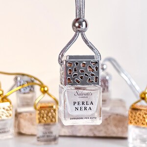 May include: A silver car air freshener with a decorative metal cage and a clear glass bottle. The bottle contains a fragrance called "Perla Nera" by Salvati's Candle. The text on the bottle reads "Diffusore per Auto".