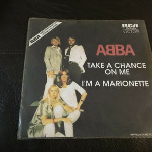 Op de afbeelding: Een zwart-witte 45-toeren plaathoes met een foto van de band ABBA. De tekst op de hoes luidt "ABBA Take a Chance on Me I'm a Marionette".