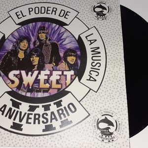 Puede incluir: Una funda de vinilo blanco con un disco de vinilo negro en su interior. La funda presenta un diseño circular con el texto "EL PODER DE LA MUSICA CON TODO" y "SWEET VII ANIVERSARIO" en un círculo blanco con una imagen morada y negra de una banda en el centro. La funda también presenta un pequeño logotipo de delfín con el texto "EL PODER DE LA MUSICA CON TODO VII ANIVERSARIO".