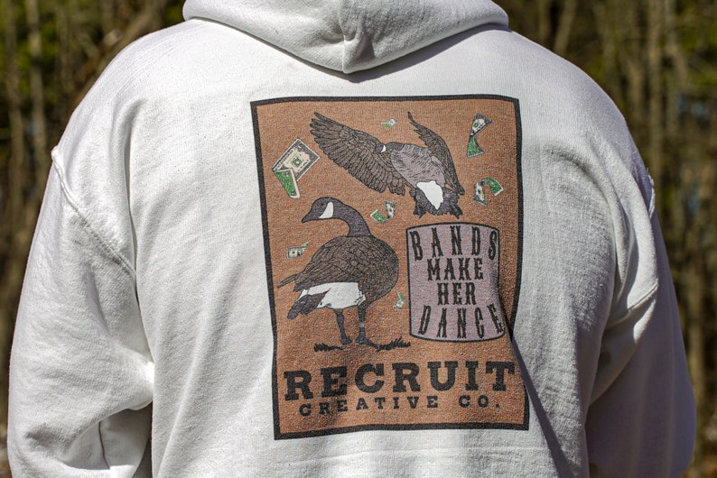 May include: White hooded sweatshirt with a brown rectangular graphic featuring two geese and the text "Bands Make Her Dance" and "Recruit Creative Co."