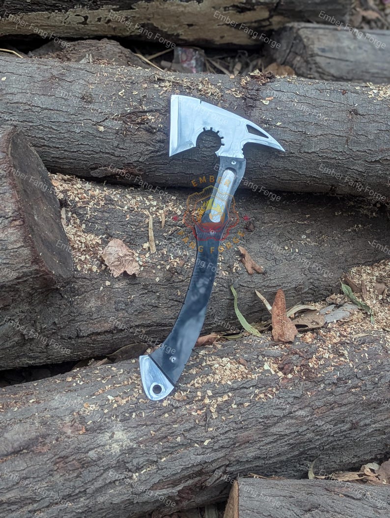 May include: A silver and black axe with a curved handle and a toothed edge on the blade. The axe head has a hammer and a circular cutout. The handle is black with silver accents. The axe is lying on a bed of wood chips and logs.