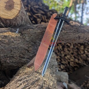 May include: A black and silver sword with a leather sheath rests on a weathered log. The sword has a black handle and crossguard, with a silver blade. The sheath is brown with a textured pattern. The background is blurred with green foliage.