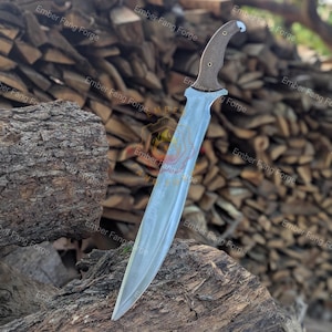 May include: A fixed-blade knife with a long, curved, silver-colored steel blade and a textured, dark brown handle secured with two metal pins. The knife is positioned vertically, with the tip resting against a piece of rough, weathered wood.