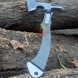 May include: A gray and silver tactical axe with a curved handle and a tomahawk-style head. The axe features a hammer on the back and a sharp blade. The axe is lying on a wooden log.