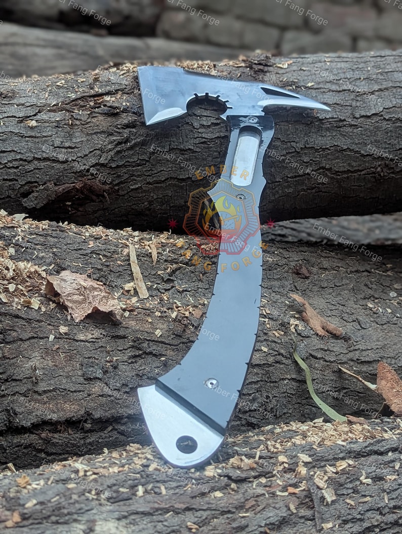 May include: A gray and silver tactical axe with a curved handle and a tomahawk-style head. The axe features a hammer on the back and a sharp blade. The axe is lying on a wooden log.