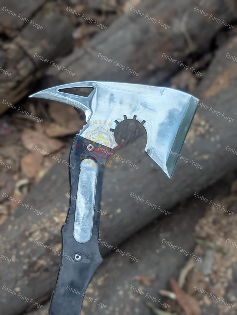 May include: A silver and black axe with a unique design. The axe head has a sharp blade, a pointed end, and a circular cutout. The handle is black with a silver insert. The text "Ember Fang Forge" is visible.