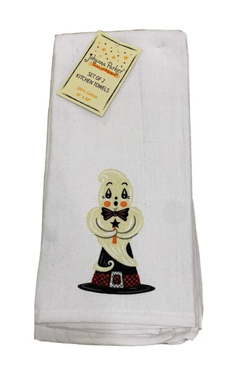 May include: A set of two white kitchen towels featuring a graphic of a ghost wearing a black hat with a red checkered band and a black bow tie, holding a star wand. The attached tag reads Johanna Parker Halloween, Set of 2 Kitchen Towels, 100% Cotton, 16" x 28".
