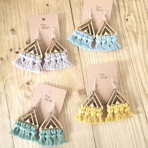 May include: Four pairs of handmade earrings with a wooden triangle design and macrame fringe in various colours: grey, blue, green, and yellow. Each pair is displayed on a brown card with the text "Knots No.29".