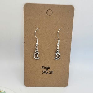 May include: Silver crescent moon dangle earrings on a brown card with the text "Knots & No. 29."