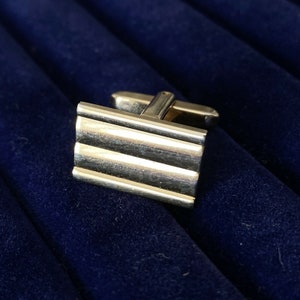 May include: Silver cufflinks with a ridged design, set against a dark blue background.
