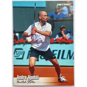 以下が含まれることがあります： アンドレ・アガシのプロテニス選手のトレーディングカード。白いシャツと黒いショートパンツを着て、テニスラケットを持っている。カードはNetproシリーズで、「アンドレ・アガシ」と「アメリカ合衆国」の文字が書かれている。