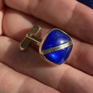 May include: Gold cufflinks with a blue square-shaped stone and a gold band across the center.
