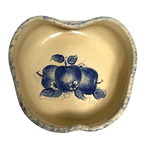 May include: A heart-shaped ceramic bowl with a blue and white apple design. The bowl has a light beige glaze and a blue rim.