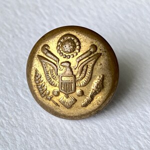 Peut inclure: Un bouton en métal doré avec le sceau des États-Unis, représentant un aigle aux ailes déployées, un bouclier à rayures verticales et une couronne de feuilles.
