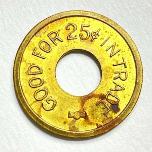 May include: A gold-colored metal token with the text "GOOD FOR 25¢ IN TRADE" around the edge. The token has a hole in the center.