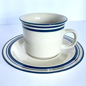 May include: A white ceramic teacup and saucer set with blue and green stripes. The cup has a handle and the saucer has a wide rim.