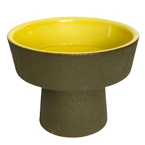 May include: A ceramic pedestal bowl with a textured, dark olive green exterior and a bright yellow interior. The bowl has a wide, shallow top and a cylindrical base, creating a modern, minimalist aesthetic.