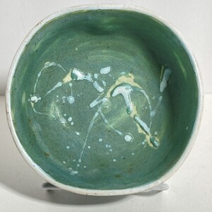 May include: A green ceramic bowl with white and yellow glaze accents. The bowl has a round shape and a smooth, glossy finish.