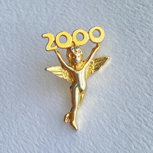 Op de afbeelding: Gouden speld met een cherub die een ring met cijfers vasthoudt die "2000" aangeeft.