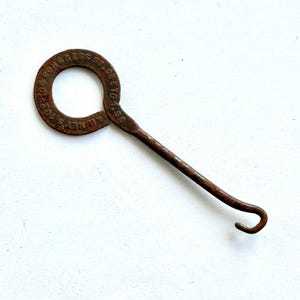 May include: A rusty metal tool with a circular handle and a curved hook. The handle has the text "IRON BRASS CO. KINNEY ST. 102" and "ST. 98 OCTO. 1. 88" embossed on it. The tool is likely vintage and used for a specific purpose.