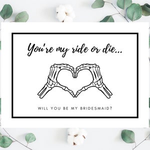May include: A white card with black text and a black skeleton hand illustration. The text reads "You're my ride or die... Will you be my bridesmaid?"