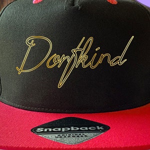 Könnte beinhalten: Schwarze und rote Baseballkappe mit einer goldenen metallischen Aufschrift "Don't Kind". Die Kappe hat einen Druckknopfverschluss und ein Etikett mit der Aufschrift "Snapback Original Wear".