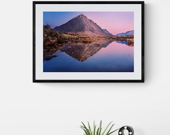May include: A framed photograph of a mountain reflected in a still lake at sunset. The mountain is a dark brown color and the lake is a light blue color. The sky is a light pink color.
