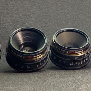 May include: Four black camera lenses with gold accents and the text "Designed by 3TP lenses".