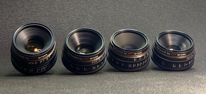 May include: Four black camera lenses with gold accents and the text "Designed by 3TP lenses".