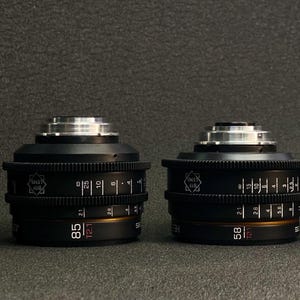 May include: Four black camera lenses with silver accents and markings. The lenses are arranged in a row from left to right, with the largest lens on the left and the smallest lens on the right. The lenses have markings indicating their focal lengths: 135mm, 85mm, 58mm, and 32mm.