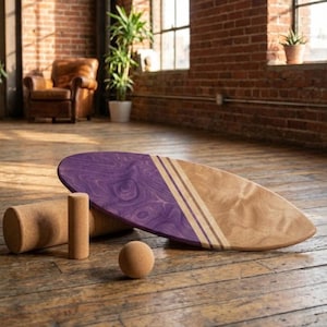 Könnte beinhalten: Ein ovales Balance-Board mit geteiltem Design, wobei eine Hälfte eine tiefviolette Holzmaserung und die andere eine natürliche helle Holzoberfläche aufweist, getrennt durch drei dünne dunkle Streifen. Dazu gehören eine Korkrolle, ein kleiner Korkzylinder und eine Korkkugel.