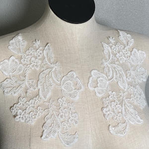 May include: Two white lace appliques with floral designs, perfect for adding a touch of elegance to wedding dresses, bridal accessories, or other craft projects.