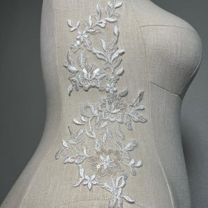 May include: White lace applique with floral and leaf designs, featuring small pearl-like embellishments.