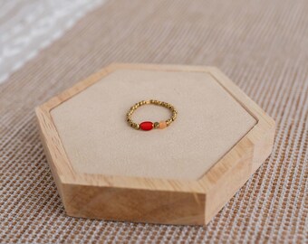 May include: A gold ring with small beads and three oval-shaped stones. The stones are red, orange, and peach.
