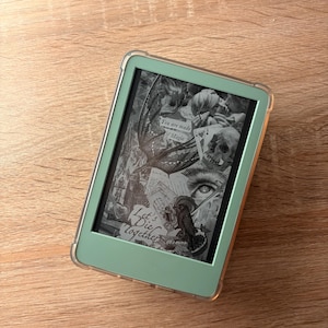 May include: A mint green e-reader with a clear protective case displays a grayscale image with text that reads "You are made of Magic" and "Let's Die Together". The image features skulls, an eye, and other gothic elements.