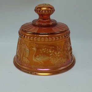 May include: A vintage amber glass butter dish with a peacock design. The dish has a domed lid with a knob on top.