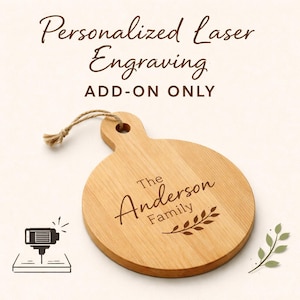 Może przedstawiać: Okrągła drewniana deska do krojenia z uchwytem, ​​z wygrawerowanym napisem "The Anderson Family" i wzorem liścia. Tekst "Personalized Laser Engraving ADD-ON ONLY" znajduje się nad deską. Maszyna do grawerowania laserowego jest pokazana po lewej stronie.