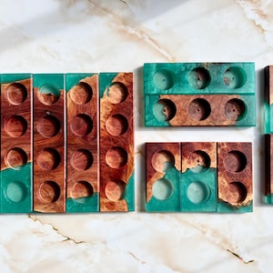 Puede incluir: Candelabros de madera con detalles de resina turquesa. Los soportes son rectangulares con hendiduras circulares para velas. La veta de la madera es visible y la resina turquesa añade color. Se muestran varios tamaños.