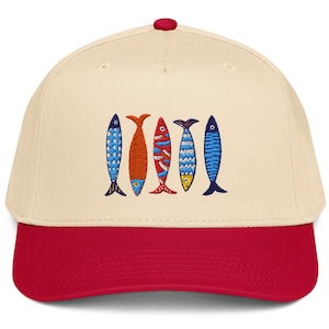 May include: A baseball cap with a cream-colored crown and a red brim. The cap features an embroidered design of five colorful fish. The fish are blue, orange, red, yellow, and blue. The cap has a red button on top.