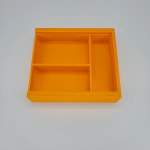 May include: An orange plastic tray with three compartments. The tray is divided into three sections, with the largest section in the center and two smaller sections on either side.
