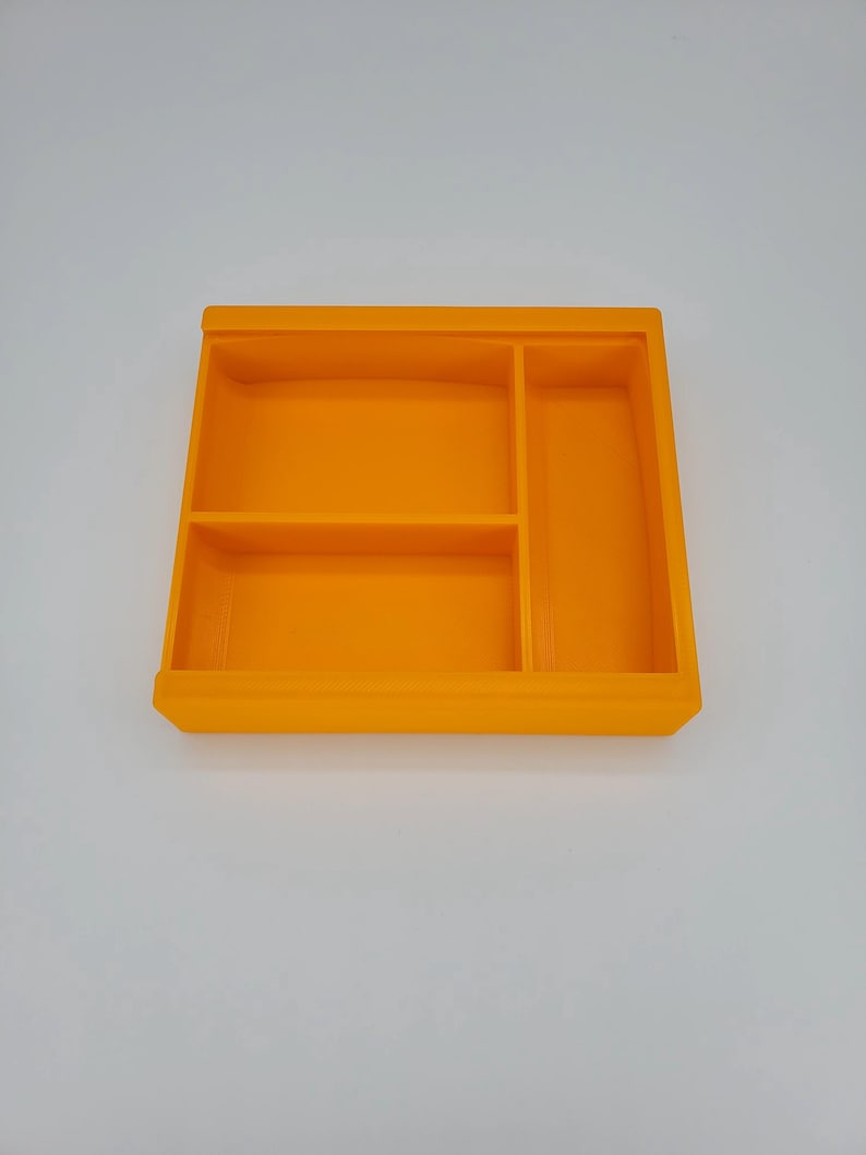 May include: An orange plastic tray with three compartments. The tray is divided into three sections, with the largest section in the center and two smaller sections on either side.