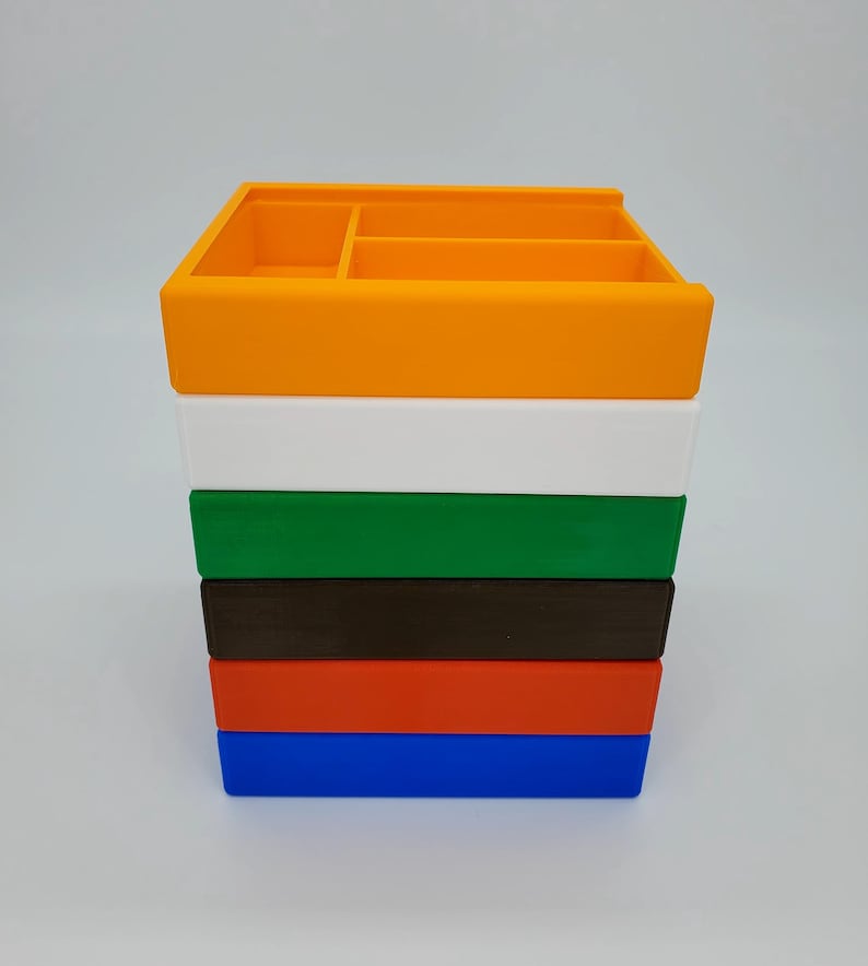 May include: A stack of six colorful plastic storage boxes. The boxes are orange, white, green, brown, red, and blue. The boxes are all the same size and shape, and they are stacked on top of each other.