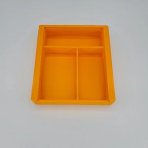 May include: Orange plastic tray with three compartments. The tray is divided into two smaller compartments and one larger compartment.