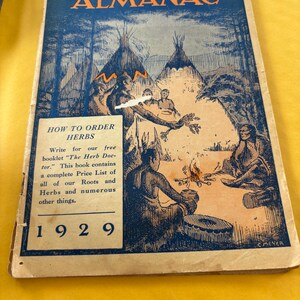 May include: A vintage 1929 softcover book titled The Herbalist Almanac. The cover features a blue and tan illustration of people near a campfire and teepees. A text box provides instructions on how to order herbs and mentions a free booklet.