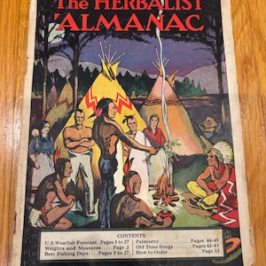 May include: A vintage paperback book titled The HERBALIST ALMANAC with a colorful cover illustration of people in a camp with teepees and a campfire. The cover includes a contents list detailing sections on weather, weights, and palmistry.